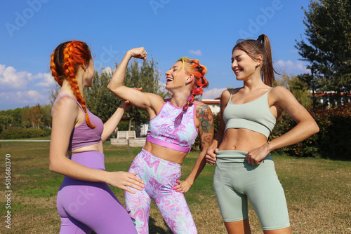 Happy woman flexing muscle standing with friends at park