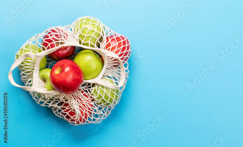 Red and green apples in mesh bag on blue