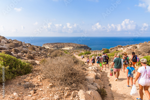 Unrecognisable tourists walk the path to Isola dei Conigli (Rabbit Island) and its beautiful beach with turquoise sea water. Lampedusa, Sicily, Italy.