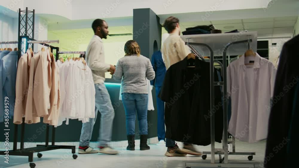 Happy customer going to fitting room to try on shirts, looking at modern clothes on racks in shopping center mall. Young woman dressing up in store, buying formal wear. Tripod shot.