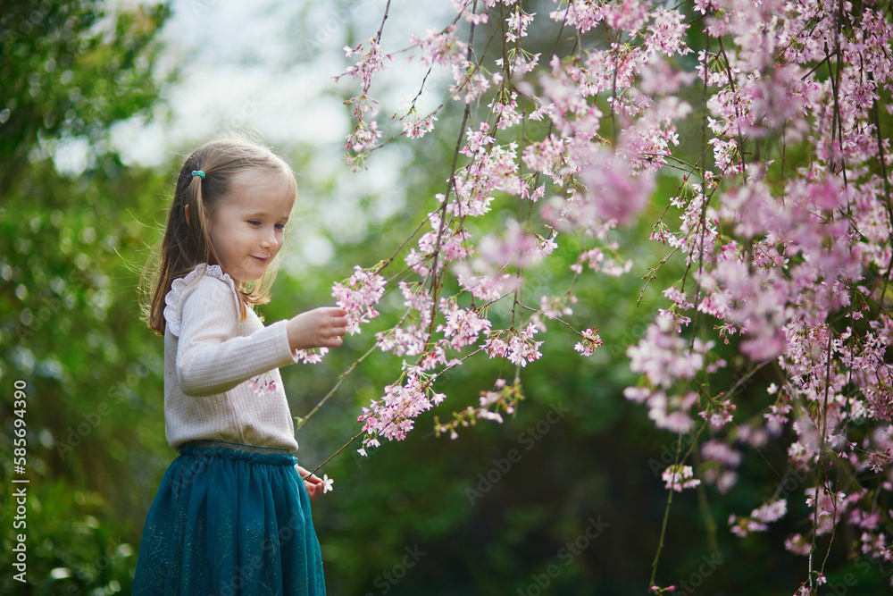 Adorable preschooler girl enjoying nice spring day in park during cherry blossom season Adorable preschooler girl enjoying nice spring day in park during cherry blossom season