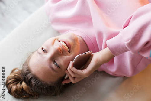 Smiling teen girl lying on sofa and talking to cellphone