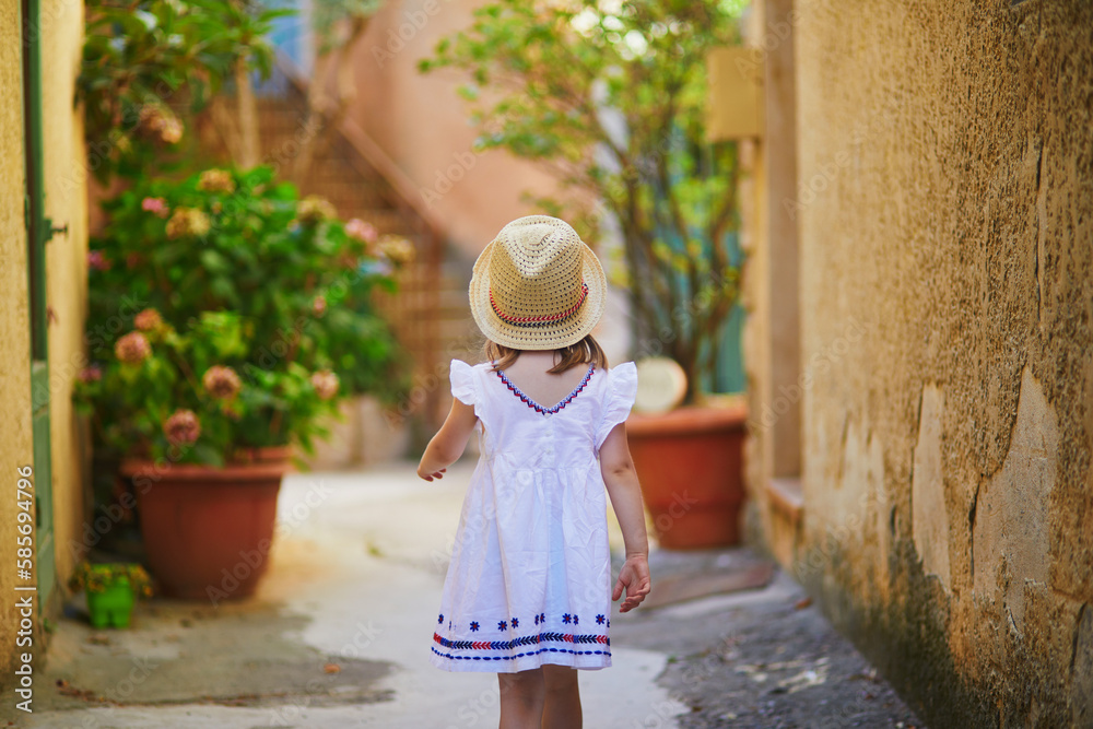 preschooler girl in white dress and straw hat on a street of Bonnieux village in Provence, France
