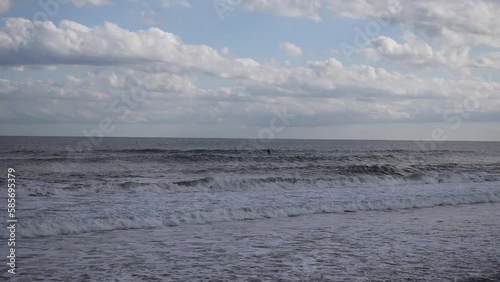青い空、白い雲、白い波。その男性はオールを使って波を漕ぎボードに立ち波に乗る。彼は波に押されて上に飛びました。