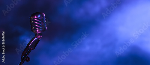 retro microphone in the dark with blue light from stage spotlights. Vintage mic on dark blue background for music live, music festival, karaoke or podcast banner with copy space.