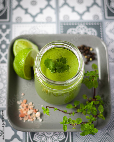 Green mint sauce in jar with herbs on grey plat.