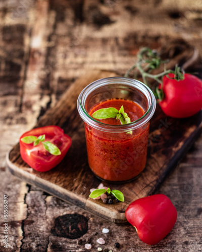 Tomato sauce with fresh tomatoes with pepper and basil on wooden background.