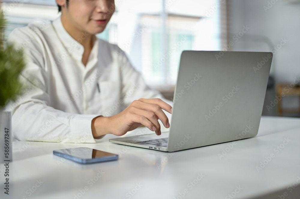 Cropped image of a handsome Asian businessman using his laptop at his desk. Cropped image of a handsome Asian businessman using his laptop at his desk.