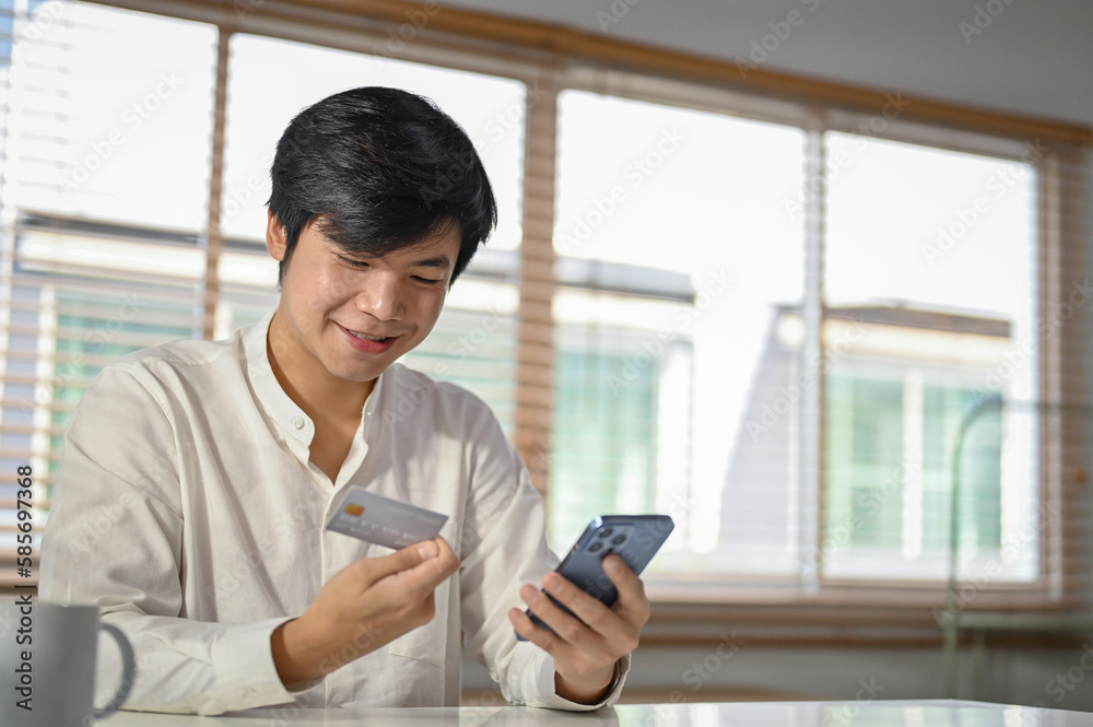 Happy Asian man using mobile banking application to transfer money or pay online bills.