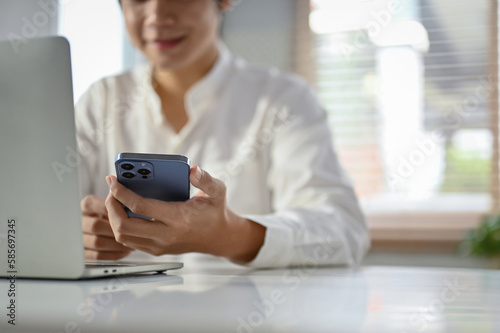 Close-up image of a happy Asian businessman using his phone at her office desk.