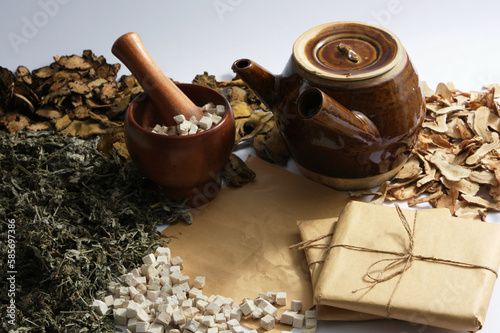 Decoction pot, mortar and pestle surrounded by dried herbs, medicine package on light background. Medicines originating from ancient China, health-protecting foods photo