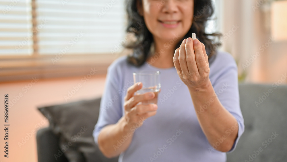 Close-up image, a happy 60-year-old retired Asian woman holding a glass of water and a pill Close-up image, a happy 60-year-old retired Asian woman holding a glass of water and a pill