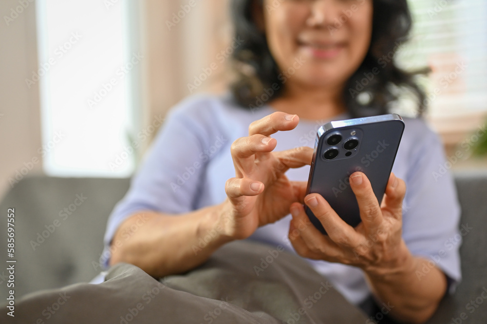 Cropped image of a happy 60-year-old retired Asian woman using her phone on a sofa Cropped image of a happy 60-year-old retired Asian woman using her phone on a sofa