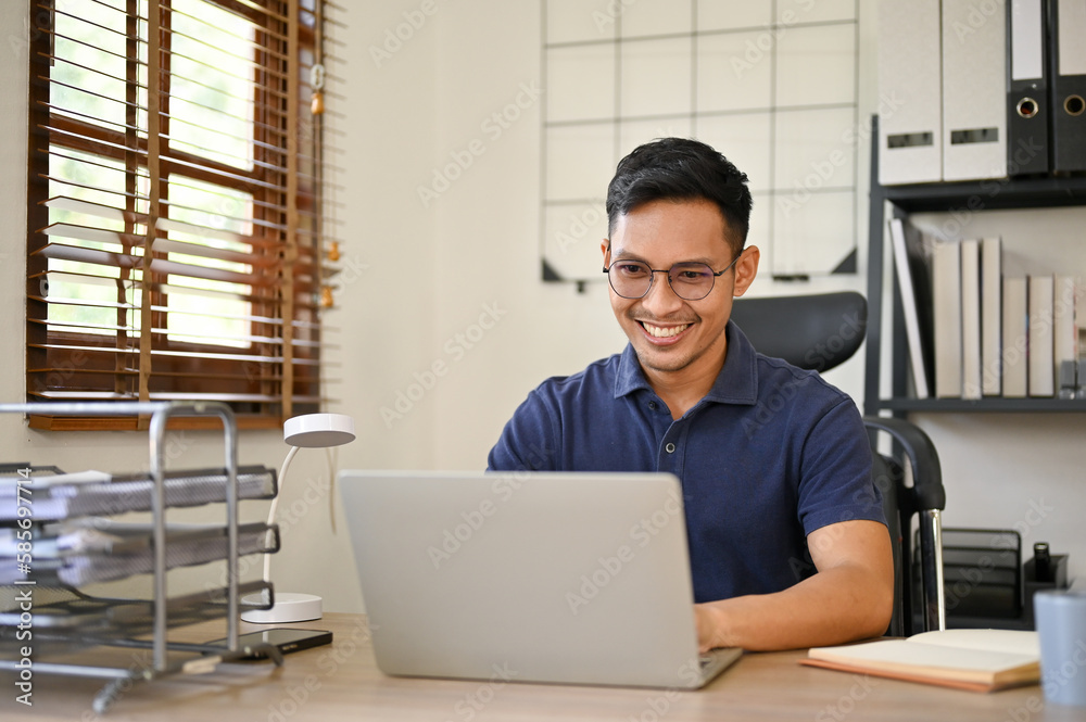 Fototapeta premium Happy Asian businessman working on his business project on laptop at his desk in the office.