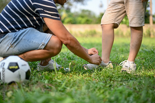 Close-up image of a caring Asian dad tying running shoe laces for his son at the backyard.