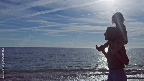 Mother carry little baby curly girl over the ocean