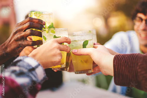 A group of multiracial friends gather at an outdoor bar and toast with mojito