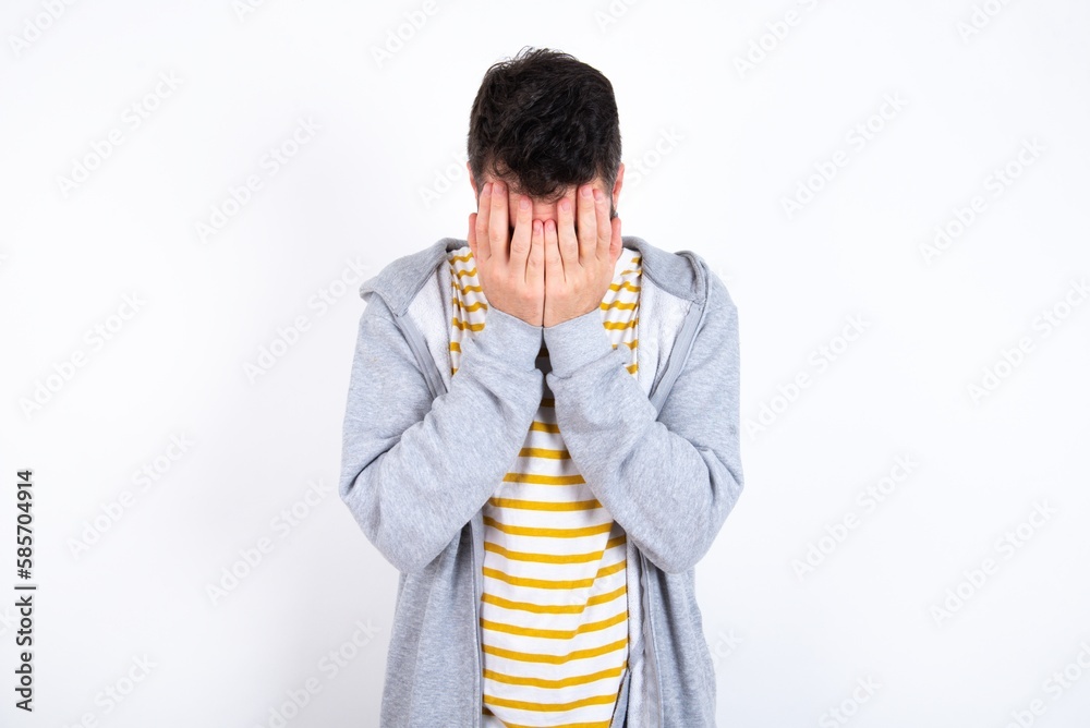 Young caucasian mán wearing trendy clothes over white background covering her face with her hands, being devastated and crying. Sad concept Young caucasian mán wearing trendy clothes over white background covering her face with her hands, being devastated and crying. Sad concept