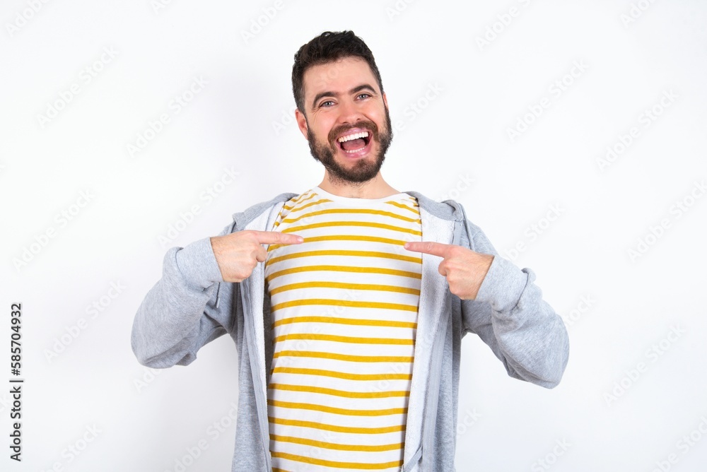 Young caucasian mán wearing trendy clothes over white background points at his body, being in good mood after going shopping and making successful purchases Young caucasian mán wearing trendy clothes over white background points at his body, being in good mood after going shopping and making successful purchases