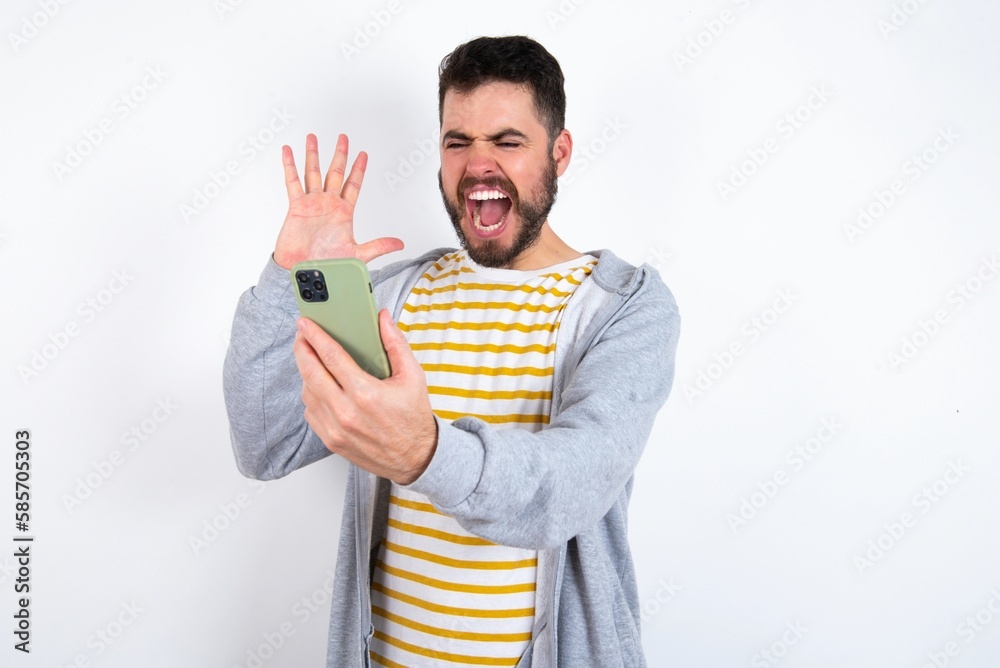 Angry Young caucasian mán wearing trendy clothes over white background screaming on the phone, having an argument with an employee. Troubles at work. Angry Young caucasian mán wearing trendy clothes over white background screaming on the phone, having an argument with an employee. Troubles at work.