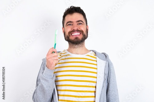 Young caucasian mán wearing trendy clothes over white background holding a toothbrush and smiling. Dental healthcare concept.