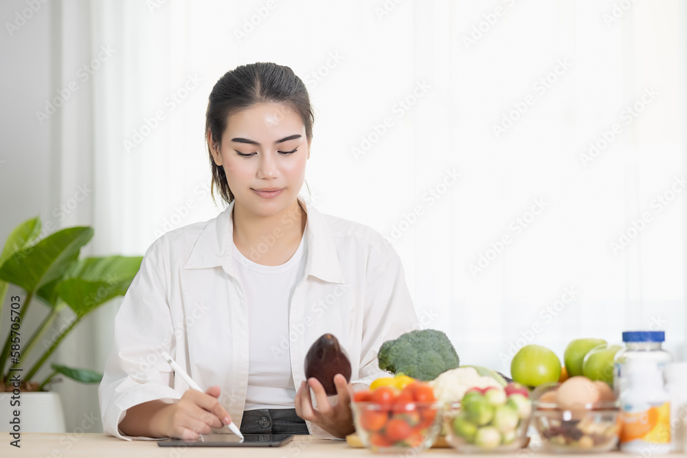 Happy female professional of nutrition healthful surrounded by a variety of fresh fruits and vegetables working on digital tablet and smiles. concept of right nutrition and diet, healthcare, diet. Happy female professional of nutrition healthful surrounded by a variety of fresh fruits and vegetables working on digital tablet and smiles. concept of right nutrition and diet, healthcare, diet.
