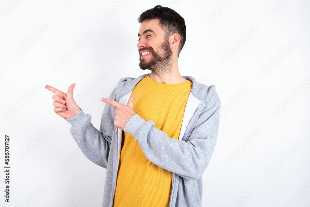 Optimistic Young caucasian mán wearing trendy clothes over white background points with both hands and  looking at empty space.