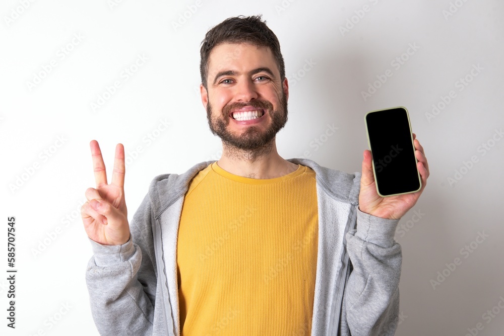 Young caucasian mán wearing trendy clothes over white background holding modern device showing v-sign Young caucasian mán wearing trendy clothes over white background holding modern device showing v-sign