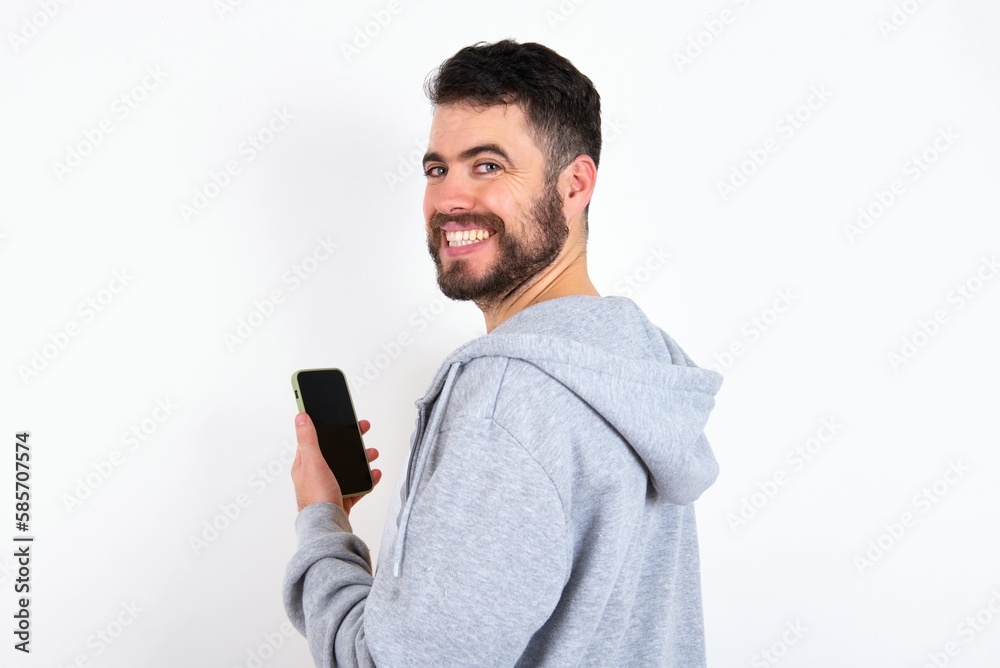Rear view photo portrait of Young caucasian mán wearing trendy clothes over white background using smartphone smiling Rear view photo portrait of Young caucasian mán wearing trendy clothes over white background using smartphone smiling