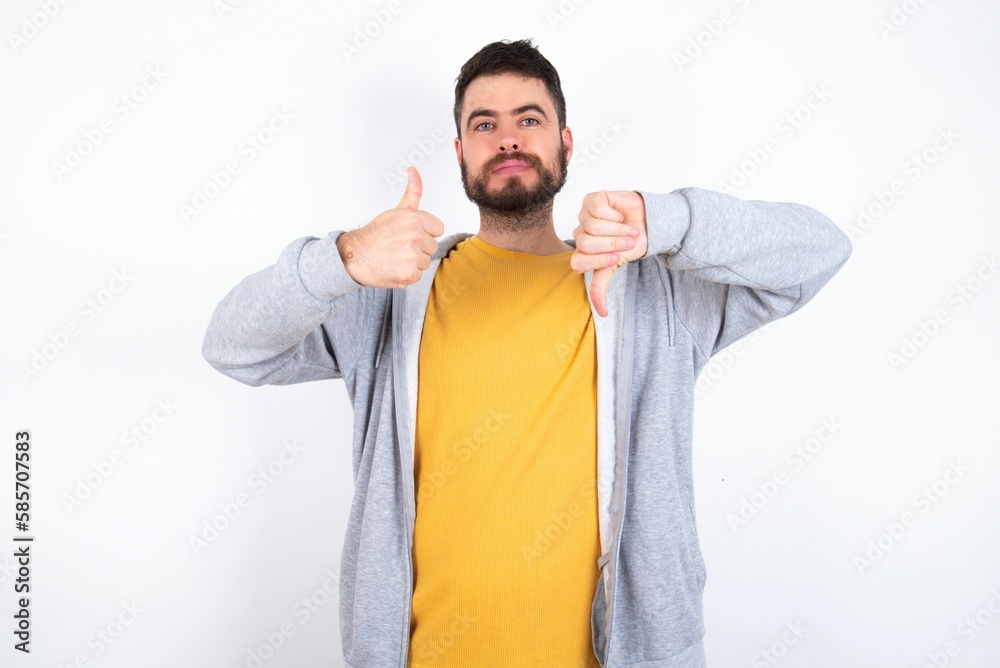 Young caucasian mán wearing trendy clothes over white background showing thumb up down sign Young caucasian mán wearing trendy clothes over white background showing thumb up down sign