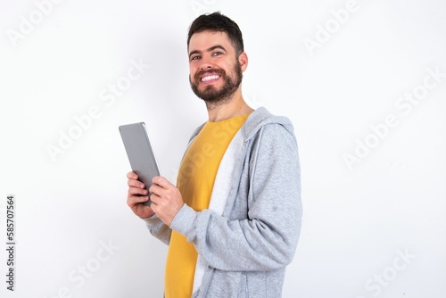 Photo of optimistic Young caucasian mán wearing trendy clothes over white background hold tablet