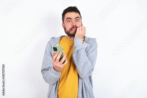 Afraid funny Young caucasian mán wearing trendy clothes over white background holding telephone and bitting nails photo