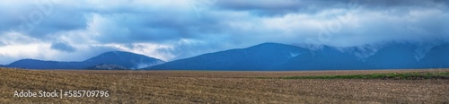 Panoramic view of mountains with storm clouds and crop fields in foreground in autumn