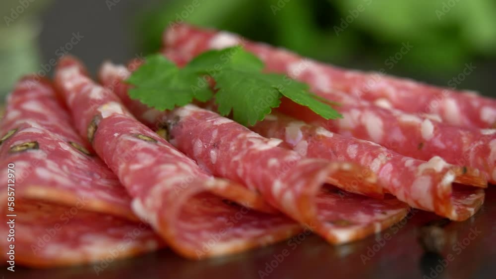 Slices smoked sausage with spices and seasonings on stone cutting board with olives and parsley. Cold cuts. Meat. Food