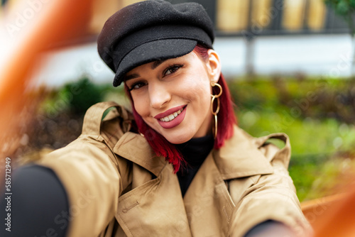 A fashion blogger takes a picture for her social networks, has red hair and is wearing a coat and a hat