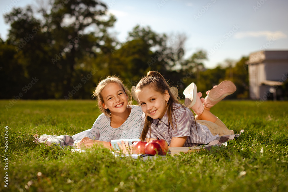 two teen girl friends looking at camera and smiling, have fun on green grass in park. School vloggers wearing casual shirts enjoying resting in summer two teen girl friends looking at camera and smiling, have fun on green grass in park. School vloggers wearing casual shirts enjoying resting in summer
