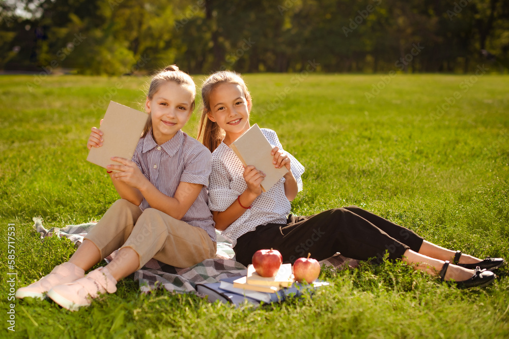 Fototapeta premium girls holding eco books in hands. cover book mockup. two excited girls reading in green summer park