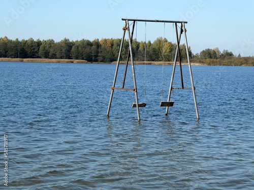 Old wooden big swing right in the water of the lake.