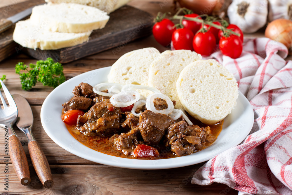 Czech traditional goulash with breaded dumpling and onion on white plate on table