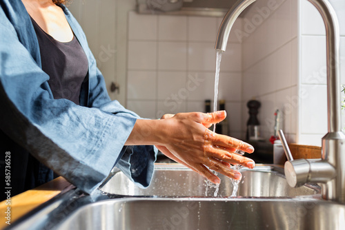 Mid section of woman washing hands in kitchen photo