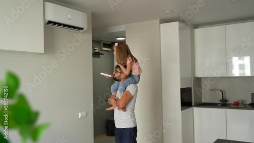 Father kept on shoulders little daughter and turn on air conditioner using remote control. Happy family adjust comfortable temperature of cooler system