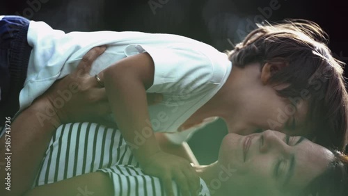 Child kissing mother on cheek outside in nature. Little boy and parent relationship showing love and affection. Motherhood concept
