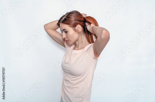 Young attractive woman fixing hair while holding hands behind head. Light T-shirt. White background.