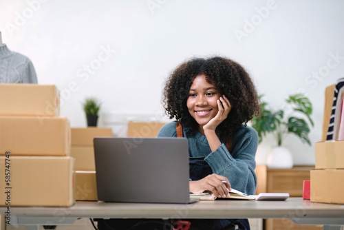 Young woman freelancer sme business online shopping look at camera with cardboard box on table at home - Business online shipping and delivery concept © wichayada