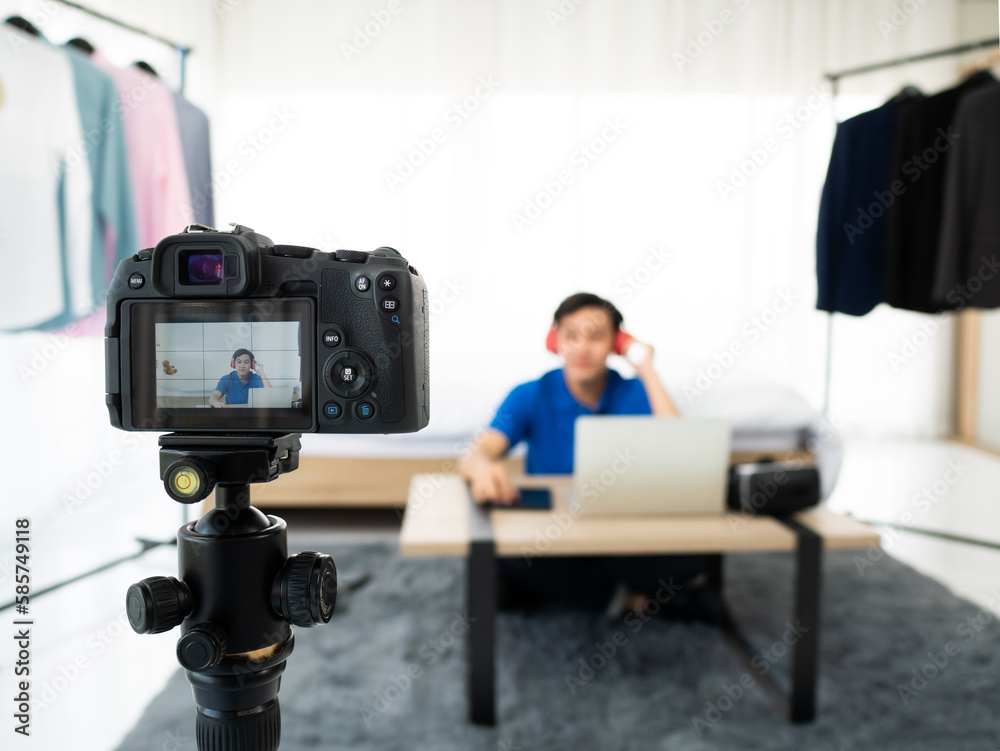 Asian entrepreneur man listening music and test sound by red headset electronic gadget while recording live video with fashion clothes background