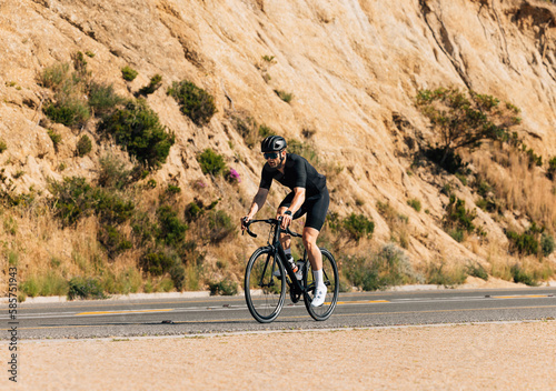 Young male in black sportswear riding a bicycle on an empty road a mountain