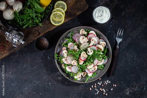 Vegetarian salad of fresh arugula, radish and mushrooms in a plate on a dark background