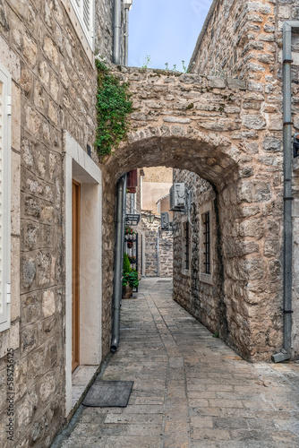Fototapeta Naklejka Na Ścianę i Meble -  Arched passage on a narrow street in the Old Town Stari Grad in Budva, Montenegro. Outdoor view of ancient buildings with stone walls, vertical