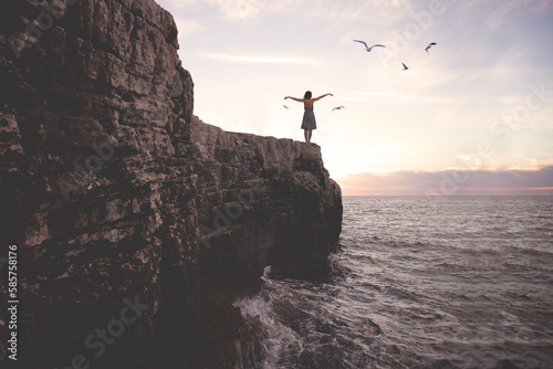 surreal woman with arms outstretched above a cliff in front of a spectacular landscape