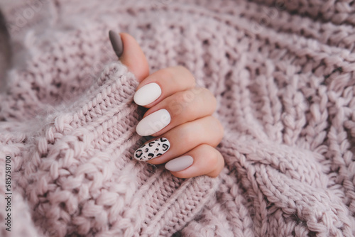 A woman's hand with a beautiful manicure holds a beige fabric. Autumn trend, beige color polishing with leopard pattern on nails with gel polish, shellac.